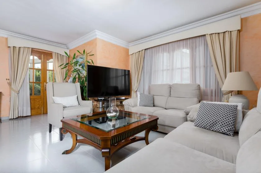 A living room with light-colored seating, a glass-topped coffee table, and a television.