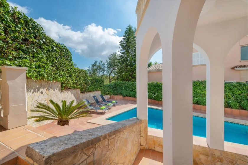 An outdoor pool beside a tiled patio, with lounge seating and arched columns.