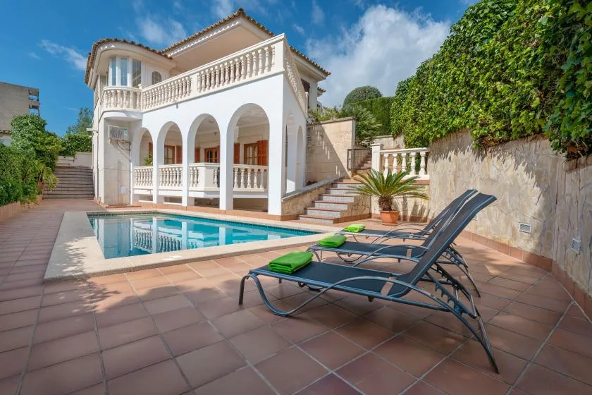 A swimming pool and lounge seating sit beside a white villa.