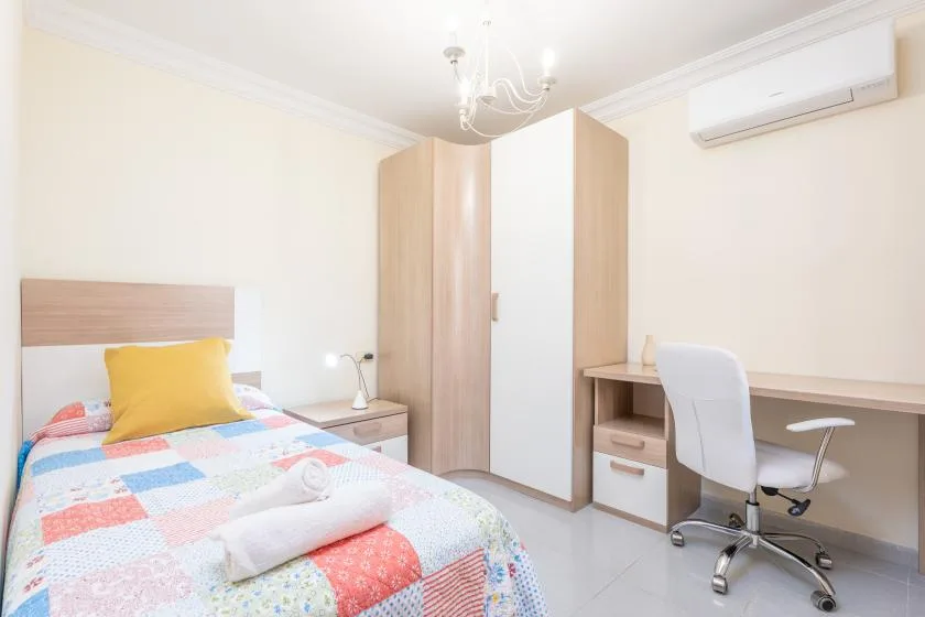 A bedroom with a colorful bed, a wardrobe, and a desk.