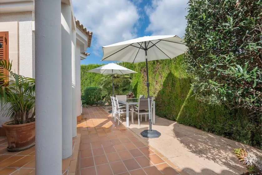 A tiled outdoor patio has a dining table and chairs beneath white umbrellas.