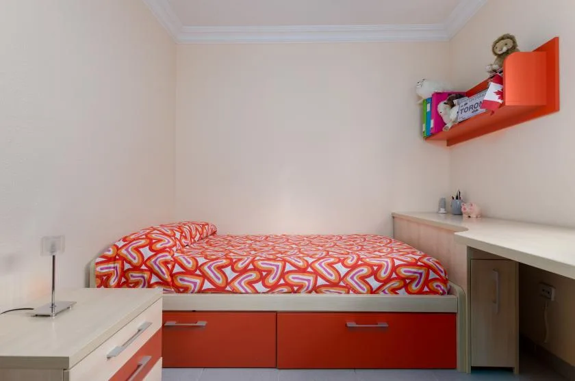 A bedroom with a bed covered in a red-and-orange patterned bedspread.