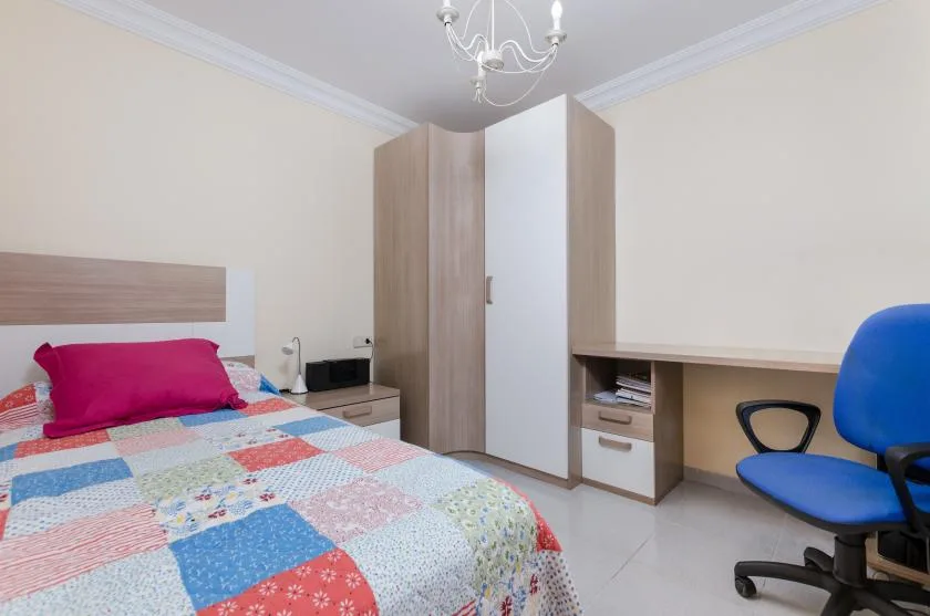 A bedroom with a colorful patchwork bedspread and a desk along the wall.