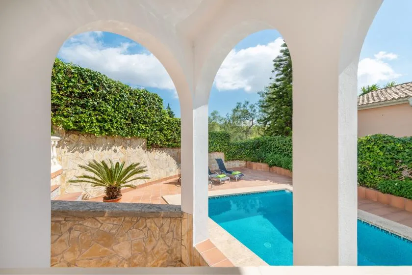 Arched openings overlook a swimming pool and a leafy patio.