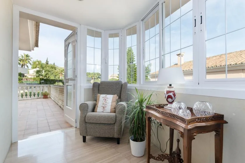 A bright sitting area with an armchair, plants, and large windows opening onto a terrace.