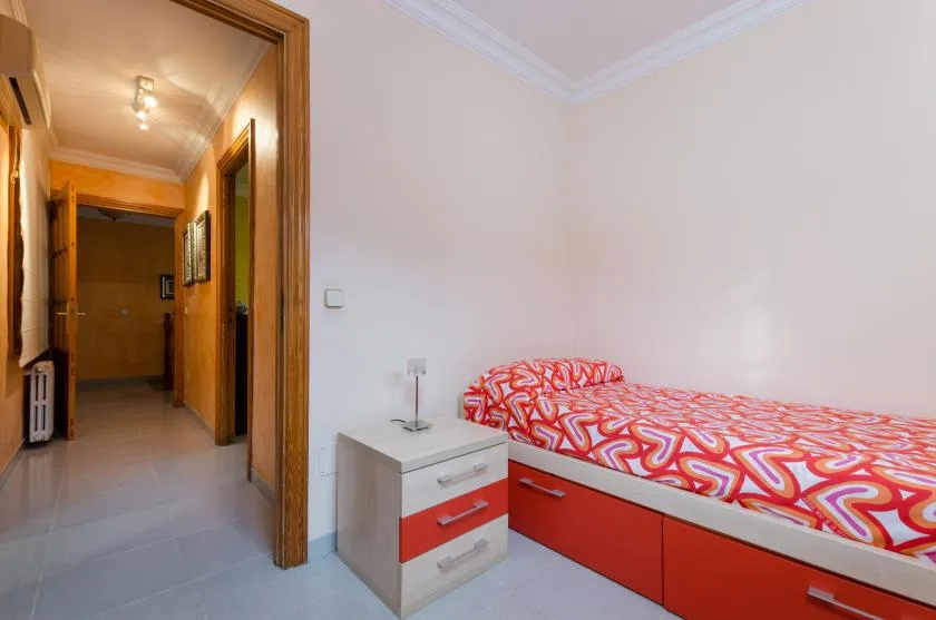 A bedroom with a single bed covered in a red and orange patterned bedspread.