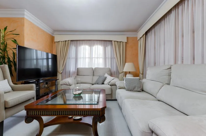 A living room with light-colored seating around a glass-topped coffee table.