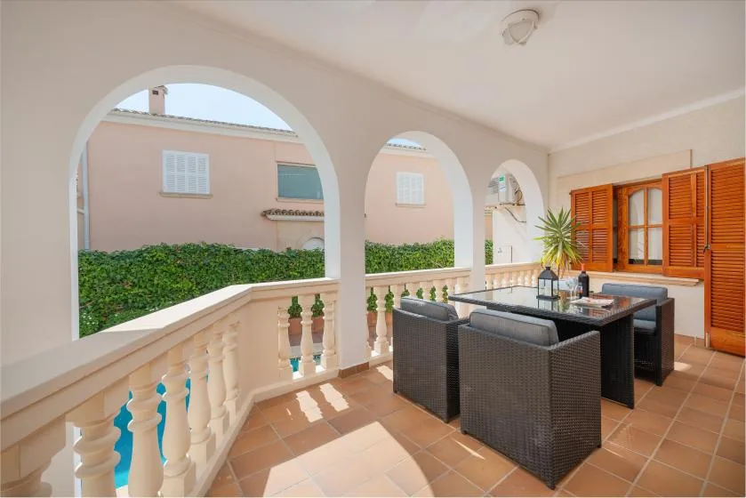 A covered patio with a dining table and seating overlooks a garden through arched openings.