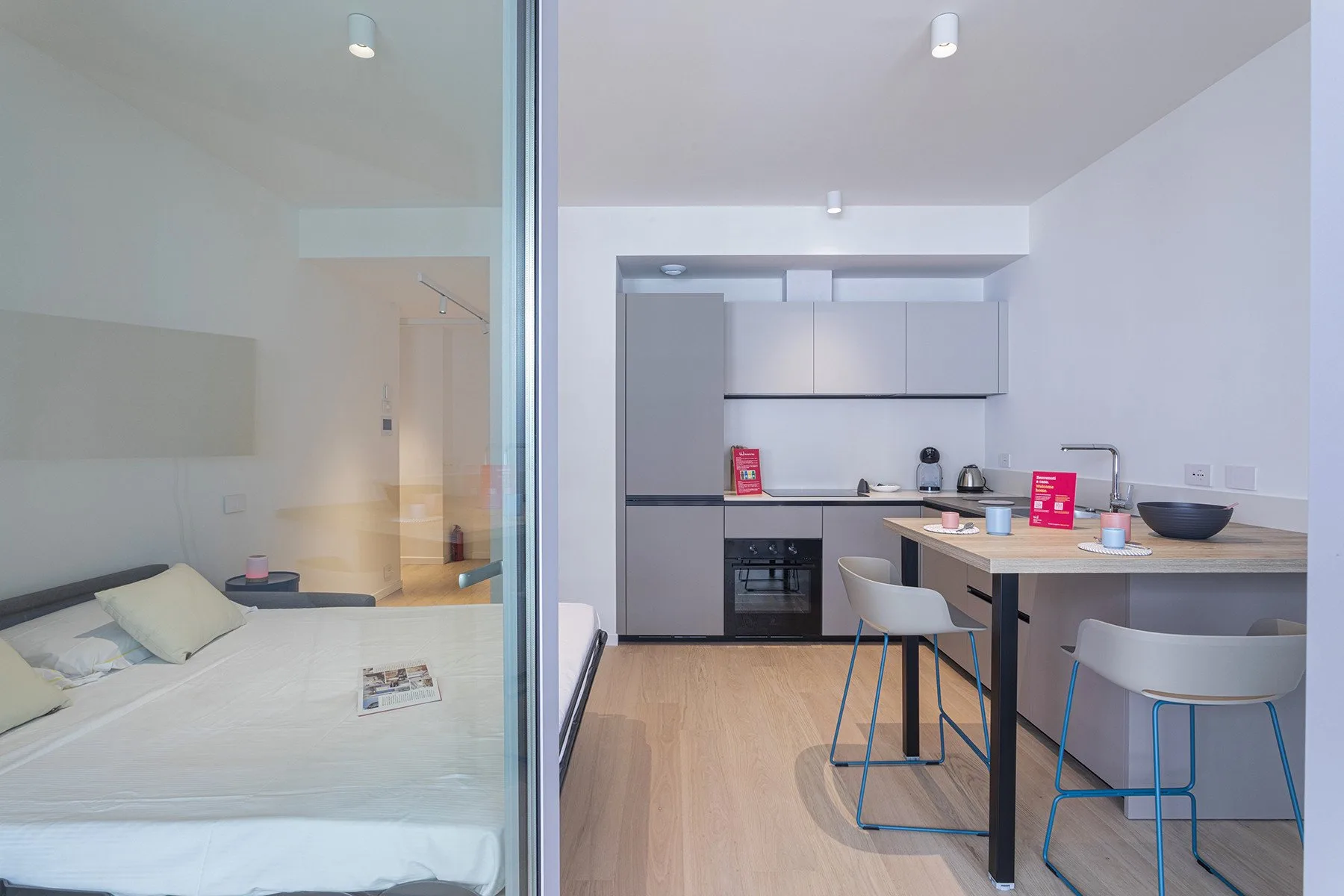 A compact kitchen and dining area with a table beside a glass-partitioned sleeping area.