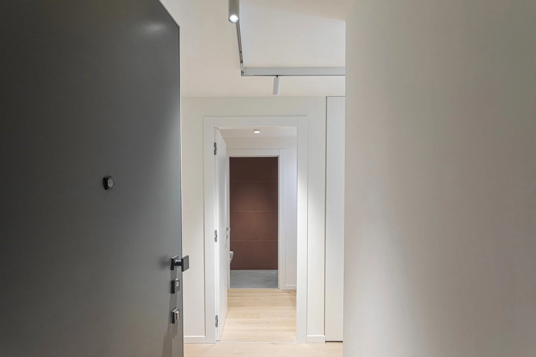 A bright hallway with an open dark door and a doorway at the far end.