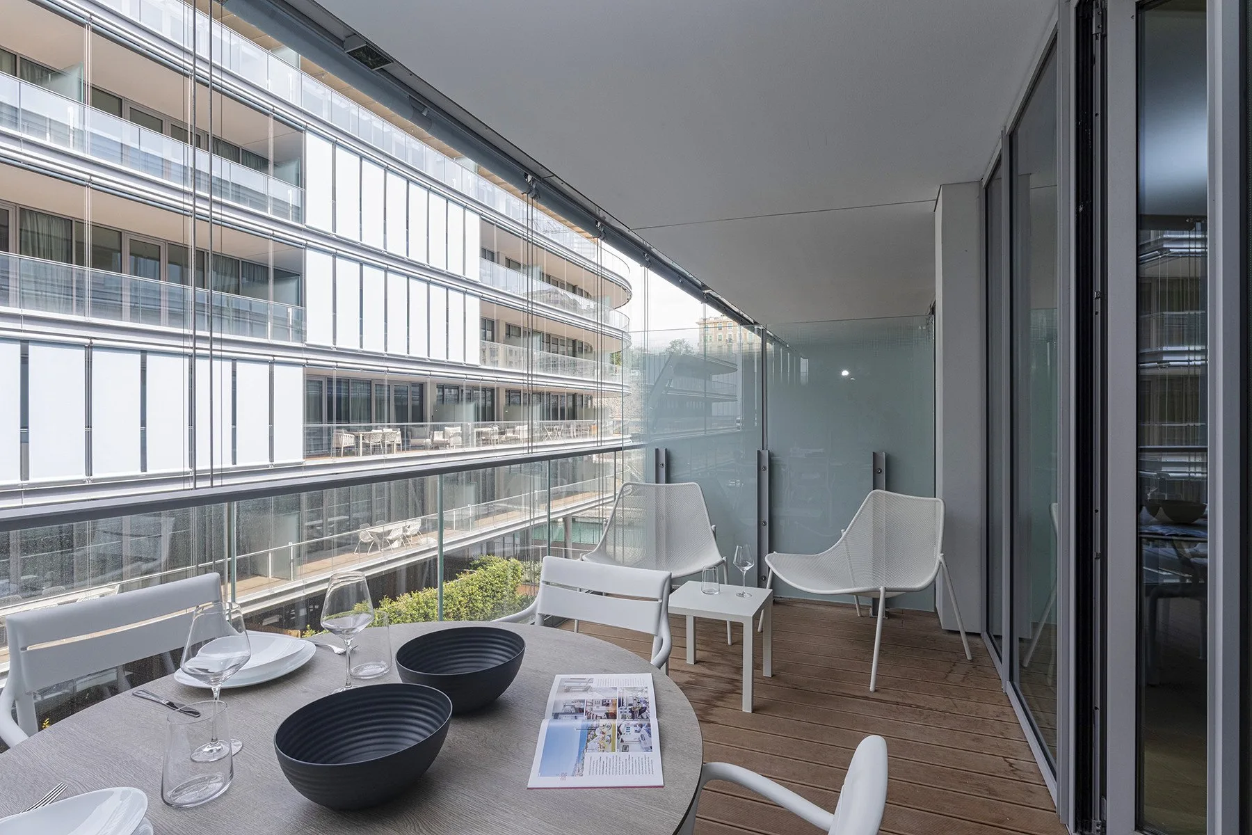 A balcony seating area has a table set with dishes beside large windows.