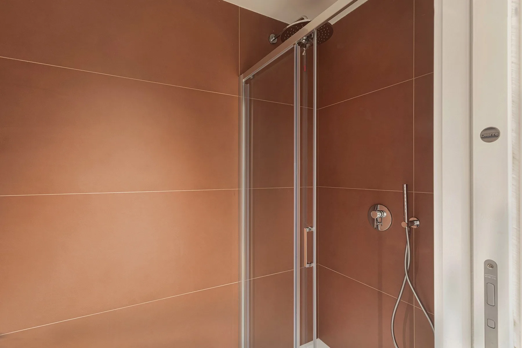 A tiled shower area with a glass shower panel and wall-mounted fixtures.