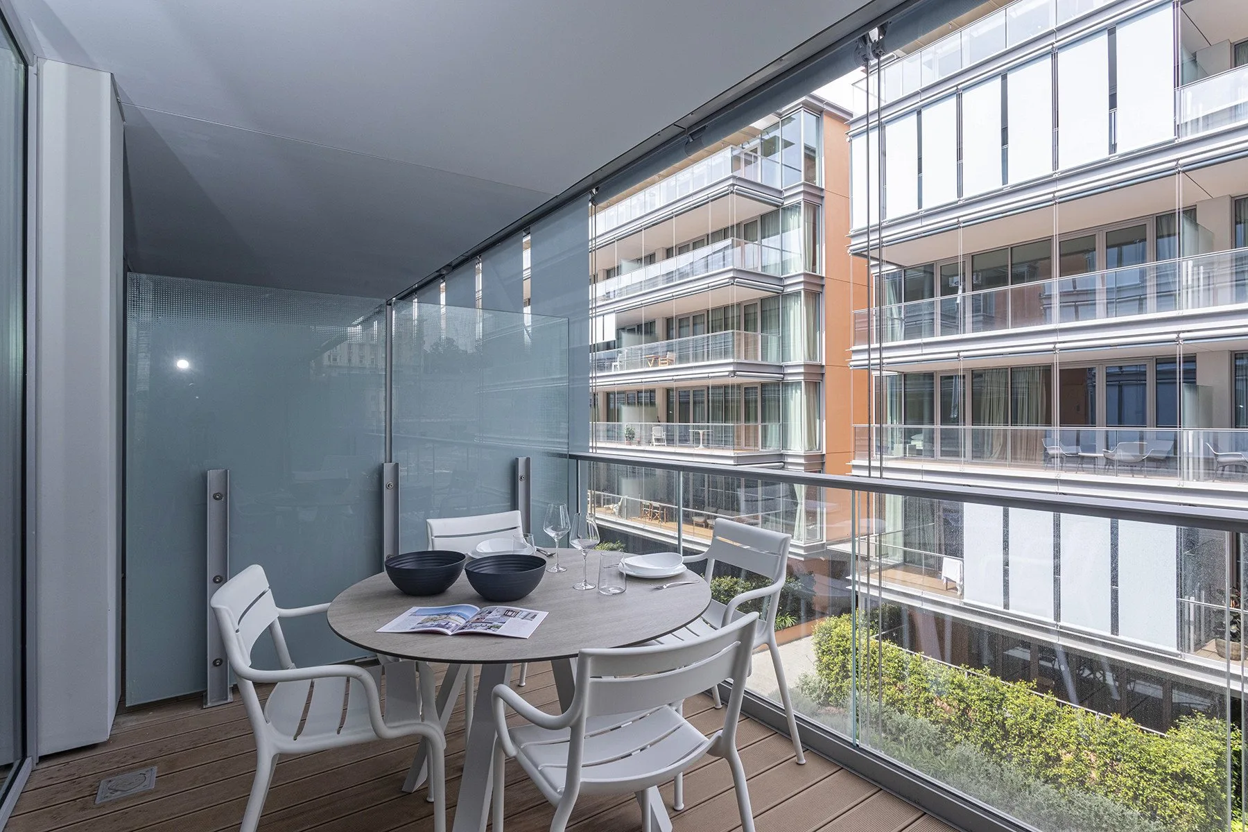 A balcony seating area overlooks a modern building through glass railings.