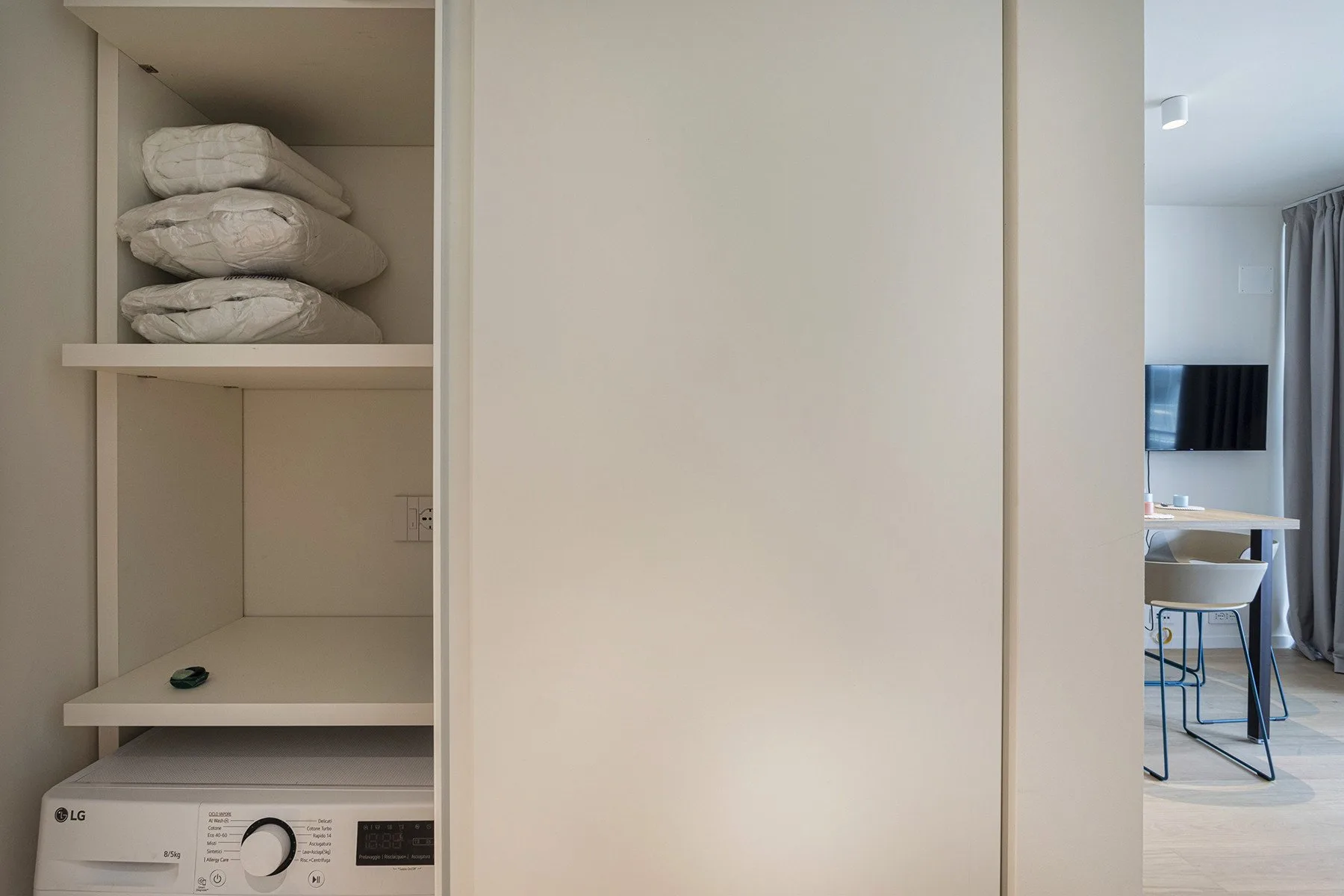 A laundry area with a washing machine and folded towels on shelves.