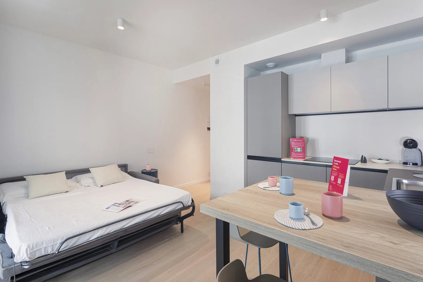 A bright bedroom with a bed beside a compact kitchenette and dining table.