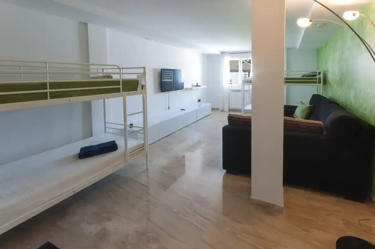 Una sala de estar luminosa con una litera, un televisor y asientos oscuros.