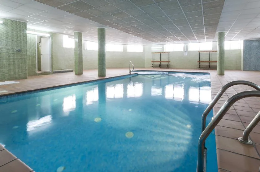 Una piscina cubierta con suelo de baldosas y pasamanos metálicos.