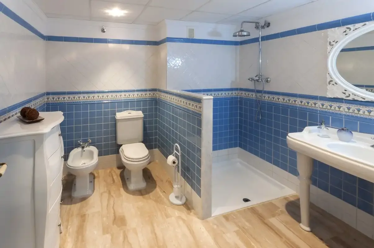 Un baño con ducha, inodoro, bidé y lavabo, decorado con azulejos azules.