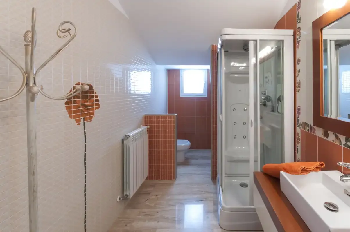 Un baño con azulejos, una ducha de vidrio, lavabo y radiador.