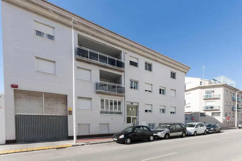 Un edificio blanco de apartamentos con balcones da a una calle con coches estacionados.