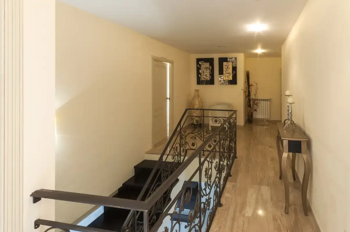 Un pasillo interior con una barandilla decorativa y cuadros enmarcados.