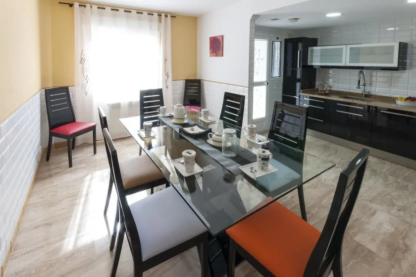 Un comedor con una mesa de vidrio y sillas está junto a una cocina abierta.