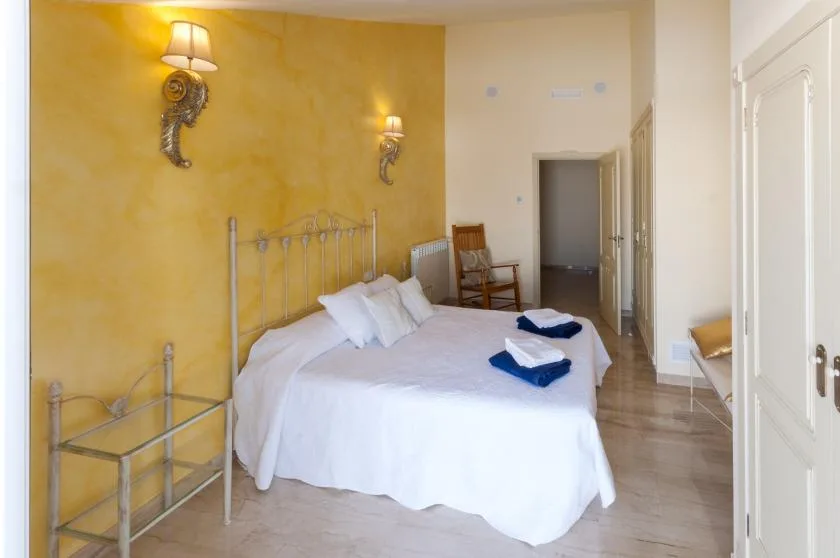 Un dormitorio con una cama blanca, cabecero metálico y pared amarilla.