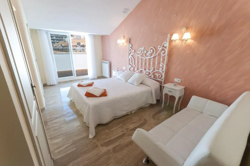 Un dormitorio con una cama blanca, un cabecero ornamentado y asientos claros.