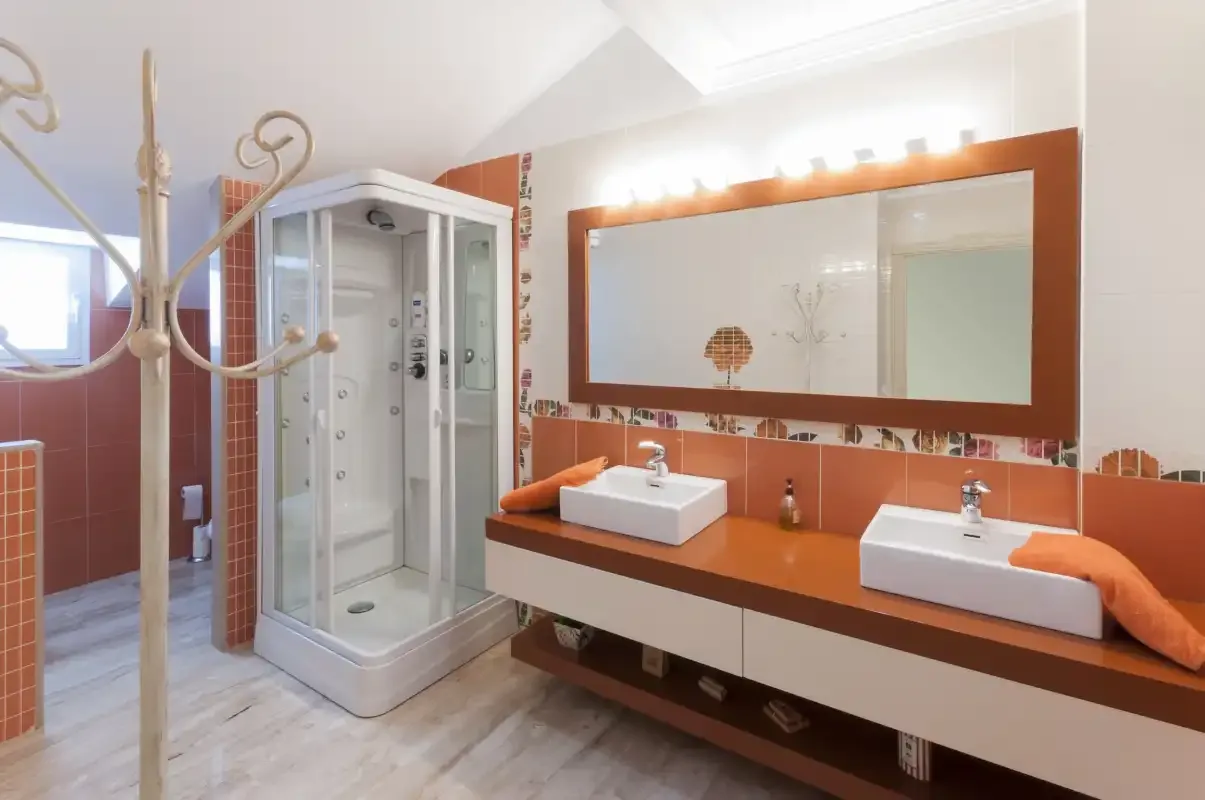 Un baño con ducha de cristal, dos lavabos y un espejo amplio.