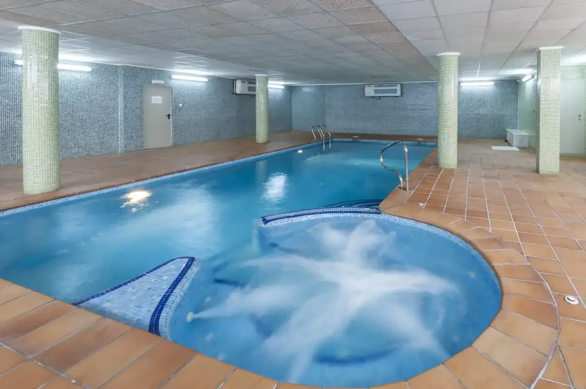 Una piscina cubierta junto a una bañera de hidromasaje con burbujas.