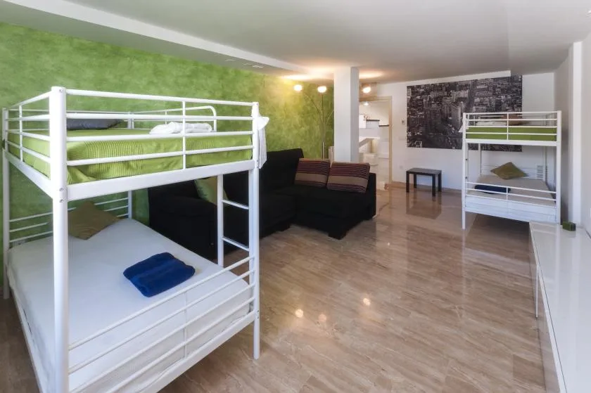 Una habitación con literas blancas, una zona de asientos oscura y suelo pulido.
