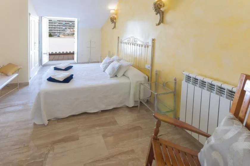 Un dormitorio con una cama bien arreglada, una mesita y asientos de madera.