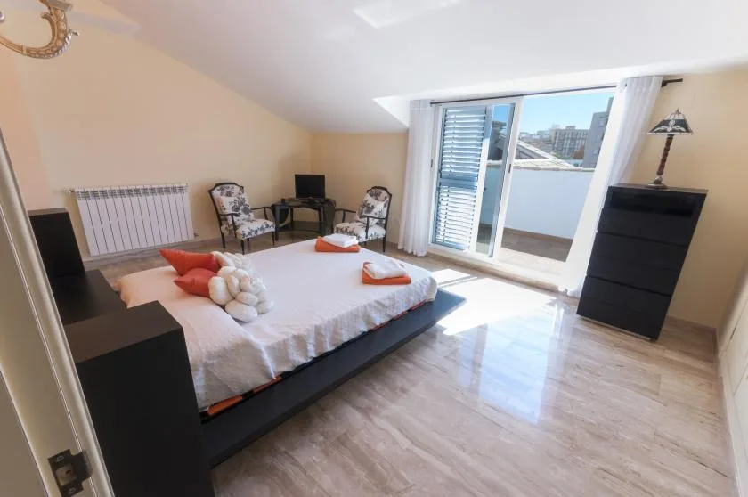 Un dormitorio con una cama, dos sillas y una puerta de vidrio que da a un balcón.