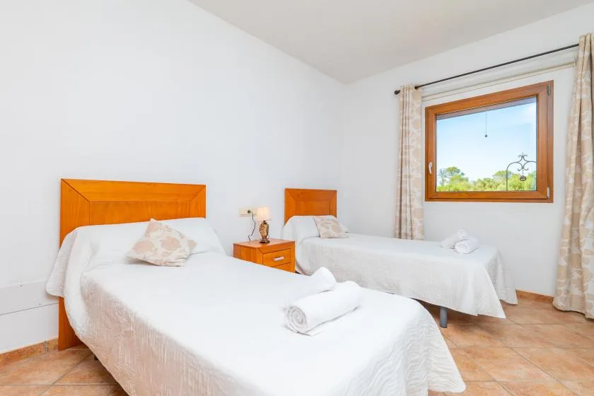 A bright bedroom with two beds and a window overlooking greenery.