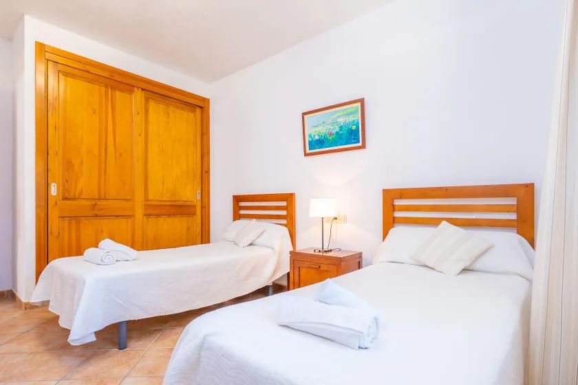 A bright bedroom with two beds, wooden wardrobes, and a bedside table.
