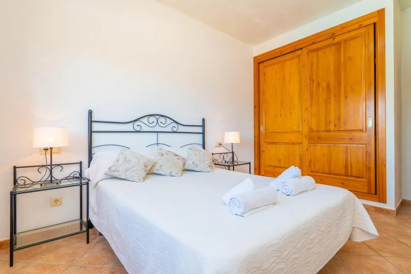 A bedroom with a white bed, dark metal headboard, and wooden wardrobe.