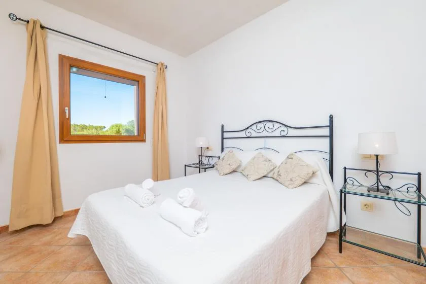 A bright bedroom with a white bed, bedside tables, and a window with curtains.