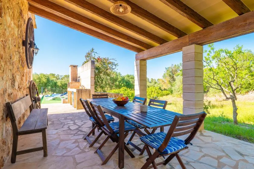 A covered outdoor dining area with a long table and chairs overlooks a leafy garden.