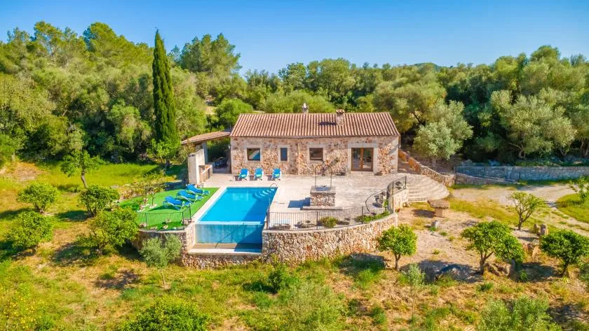 A stone house and swimming pool sit among trees and open greenery.
