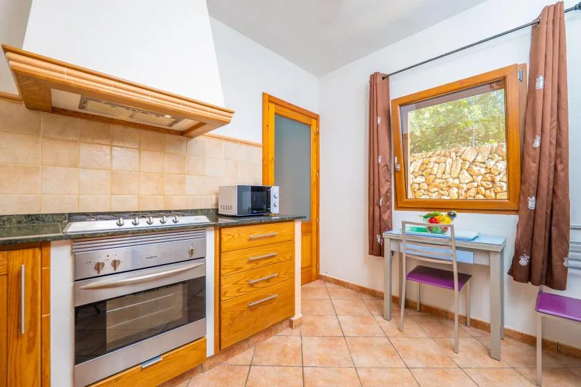 A kitchen with wooden cabinets, a stovetop, and a dining table by the window.