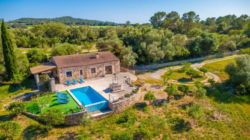 A stone house with a swimming pool sits amid green countryside.