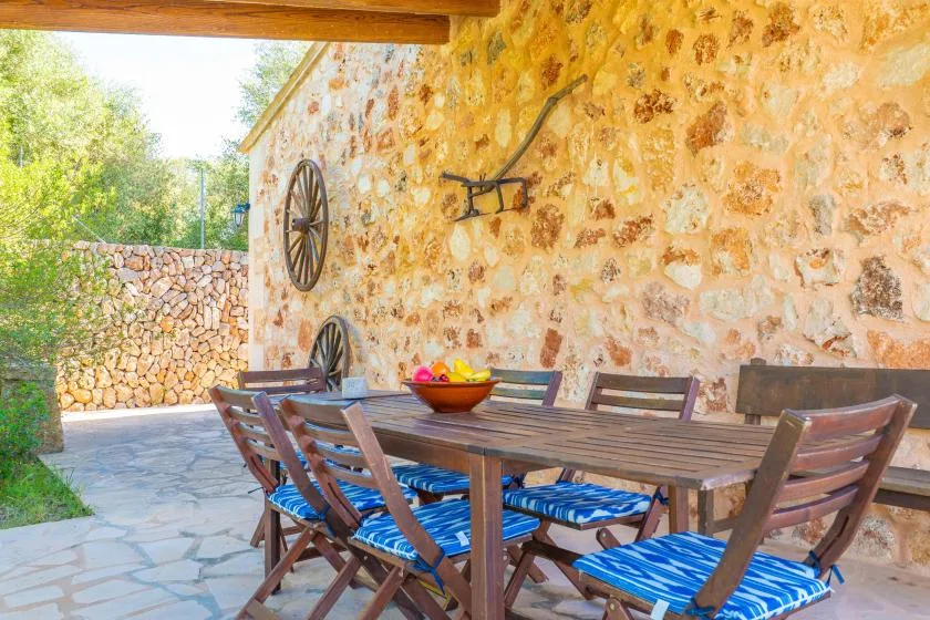 An outdoor dining area with a wooden table and blue-cushioned seating beside a stone wall.