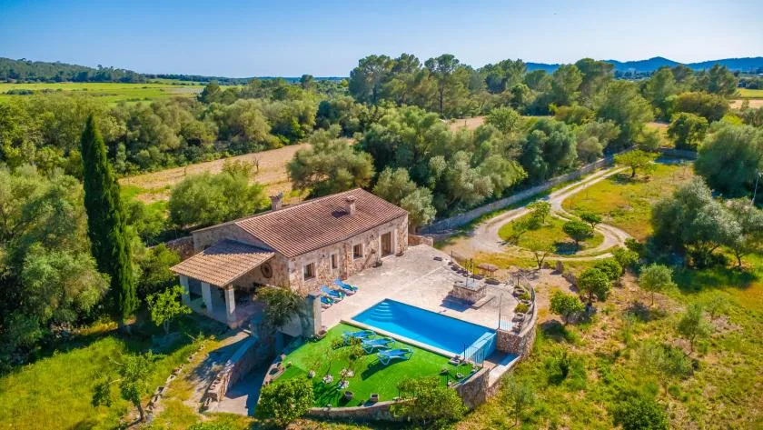 A countryside house beside a blue swimming pool, surrounded by trees and fields.