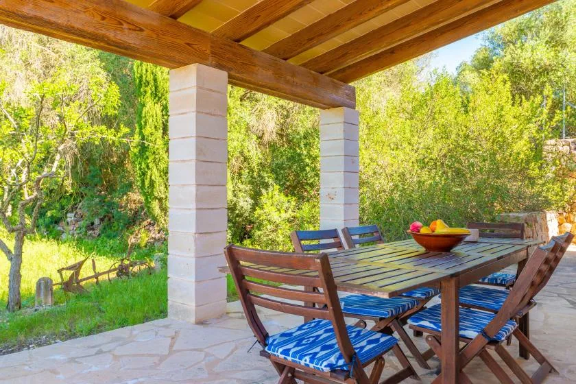 An outdoor dining area with a wooden table and chairs beneath a covered patio.
