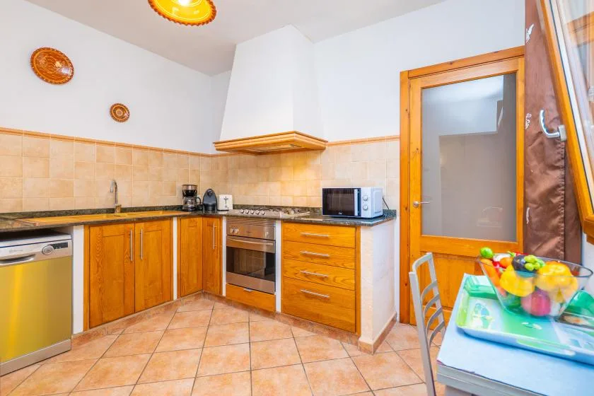 A tiled kitchen with wooden cabinets, a countertop, and a small dining table.