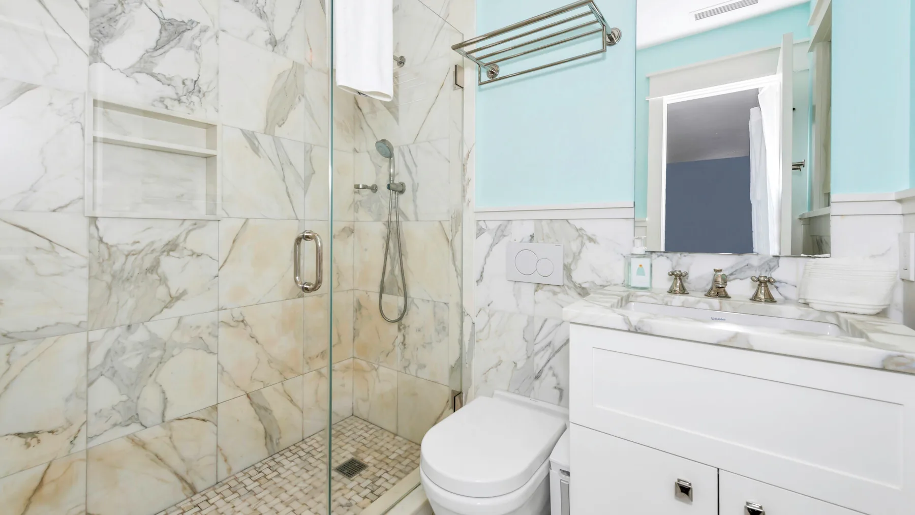 A bright bathroom with a glass shower, marble-patterned walls, and a white vanity.