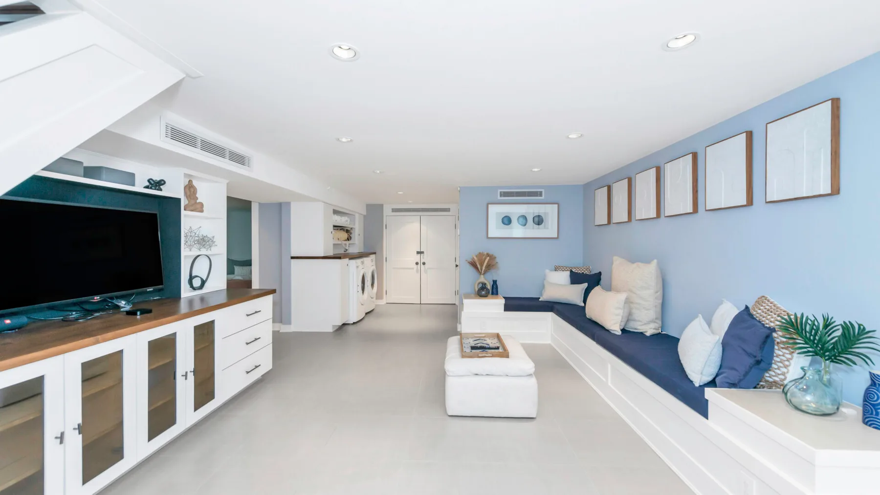 A bright living room with a long built-in seating area and entertainment cabinetry.