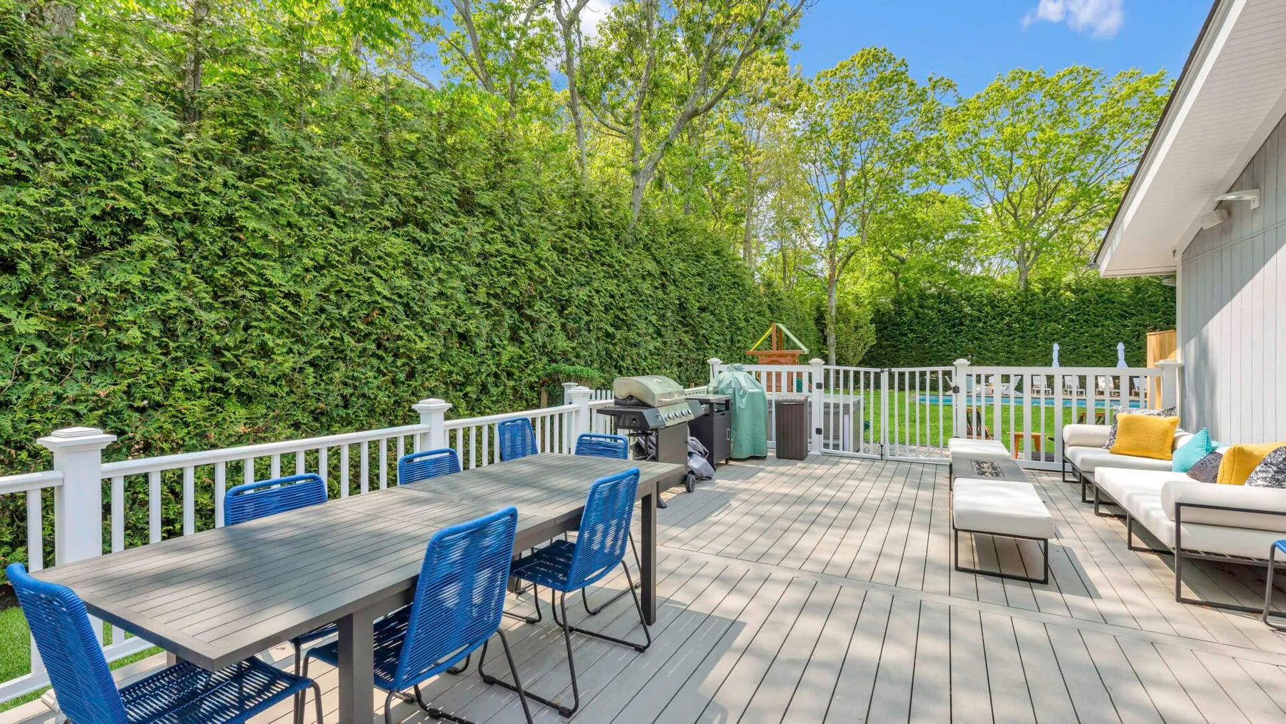 Una terraza exterior con mesa de comedor, asientos y una barandilla blanca.