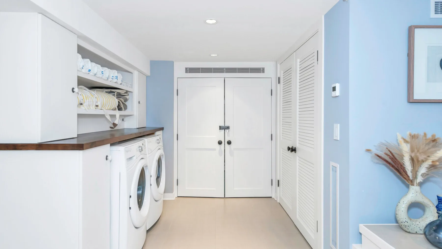 A bright laundry room with front-loading machines and white storage cabinets.
