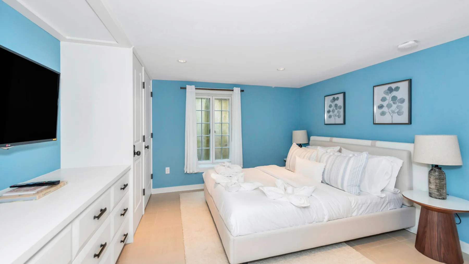 A bright bedroom with a large bed, blue walls, and a window.